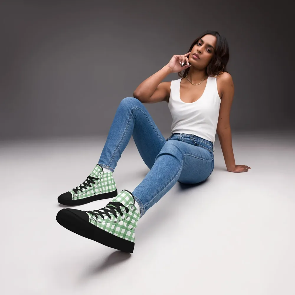 A woman sits on a studio floor in jeans and the green Gingham Sneakers, a high-top canvas shoe.